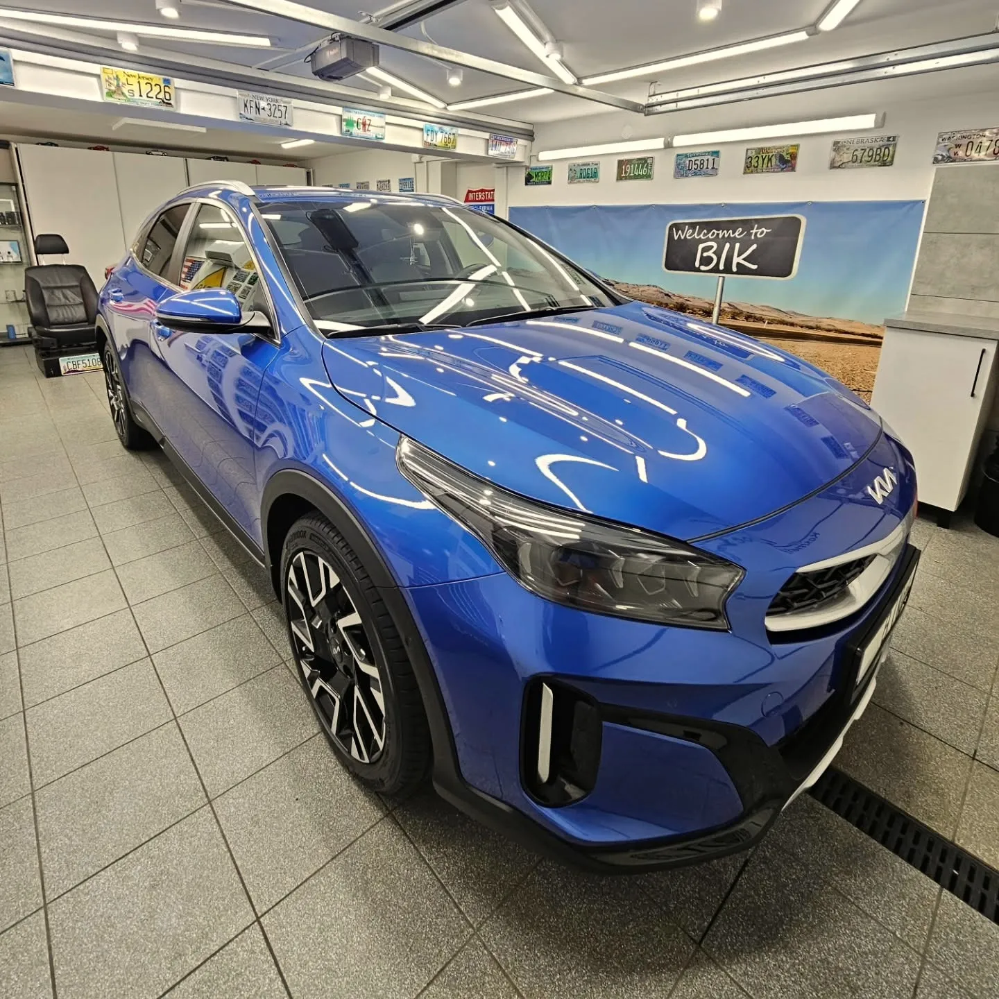 Niebieska Kia XCeed w studiu BIK, w tle ściana z tablicami z USA i tablica Welcome to BIK