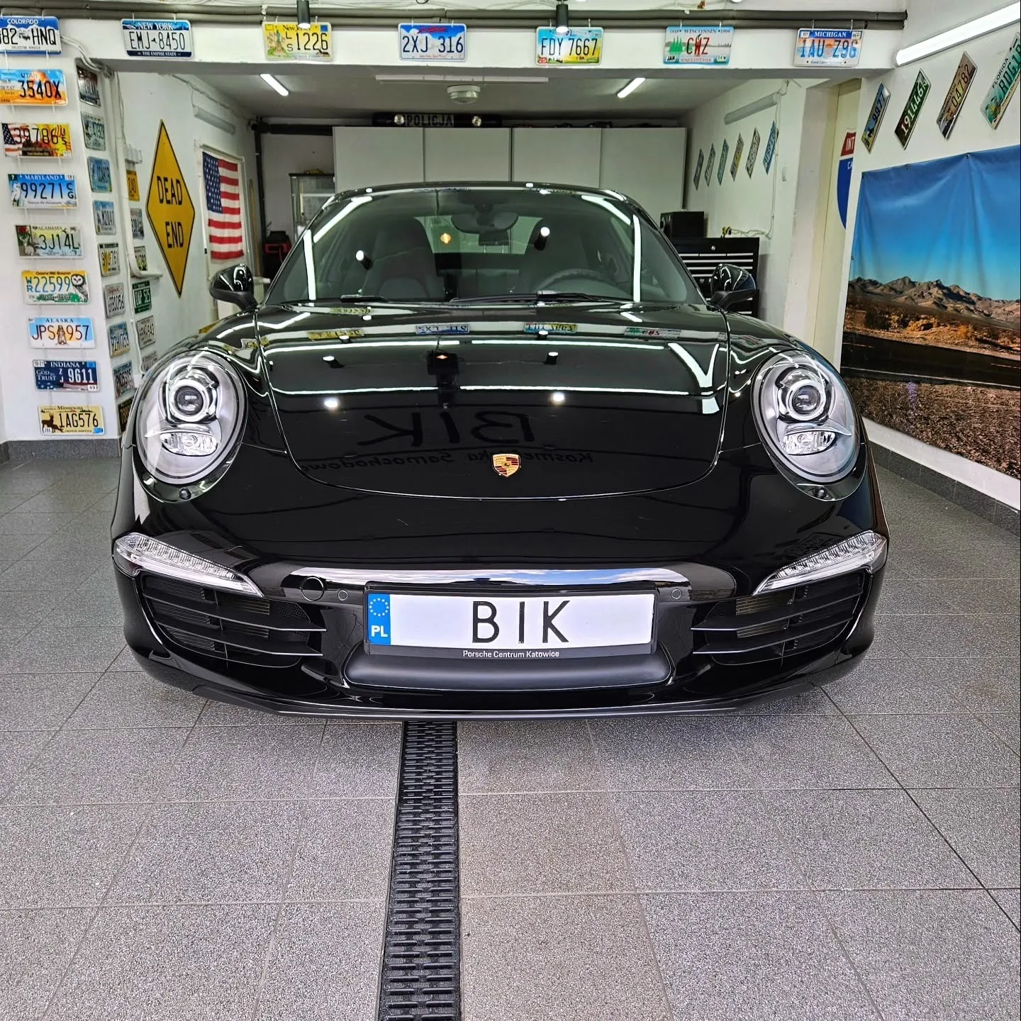 Czarne Porsche 911 od przodu w studiu BIK w Chrzanowie, w tle ściana z amerykańskimi tablicami rejestracyjnymi